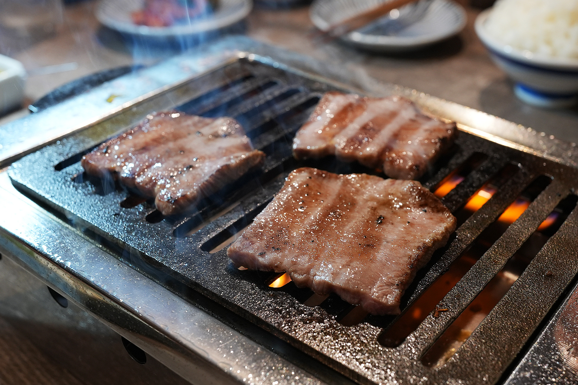 麻布苑の黒タン元を焼いているところ。網の上で4切れが焼かれ、脂が落ちて炎が上がっている