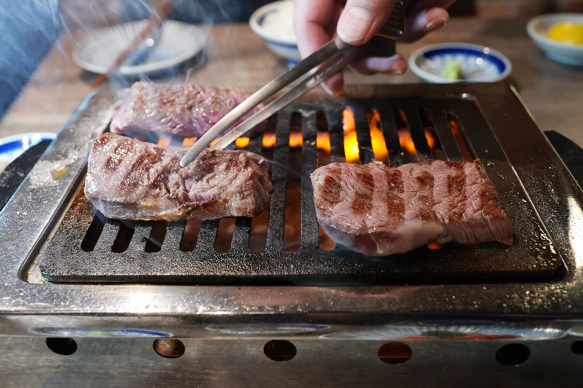 麻布苑の厚切り特上ハラミを焼いているところ。トングで肉を持ち上げ、焼き加減を見ている