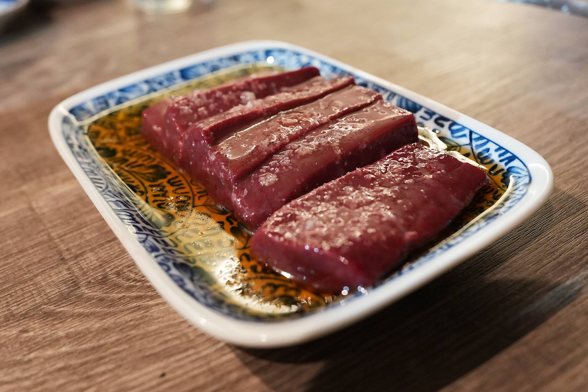 麻布苑の特上レバー。厚切りのレバーが4切れ、染付の角皿にごま油とともに盛られている