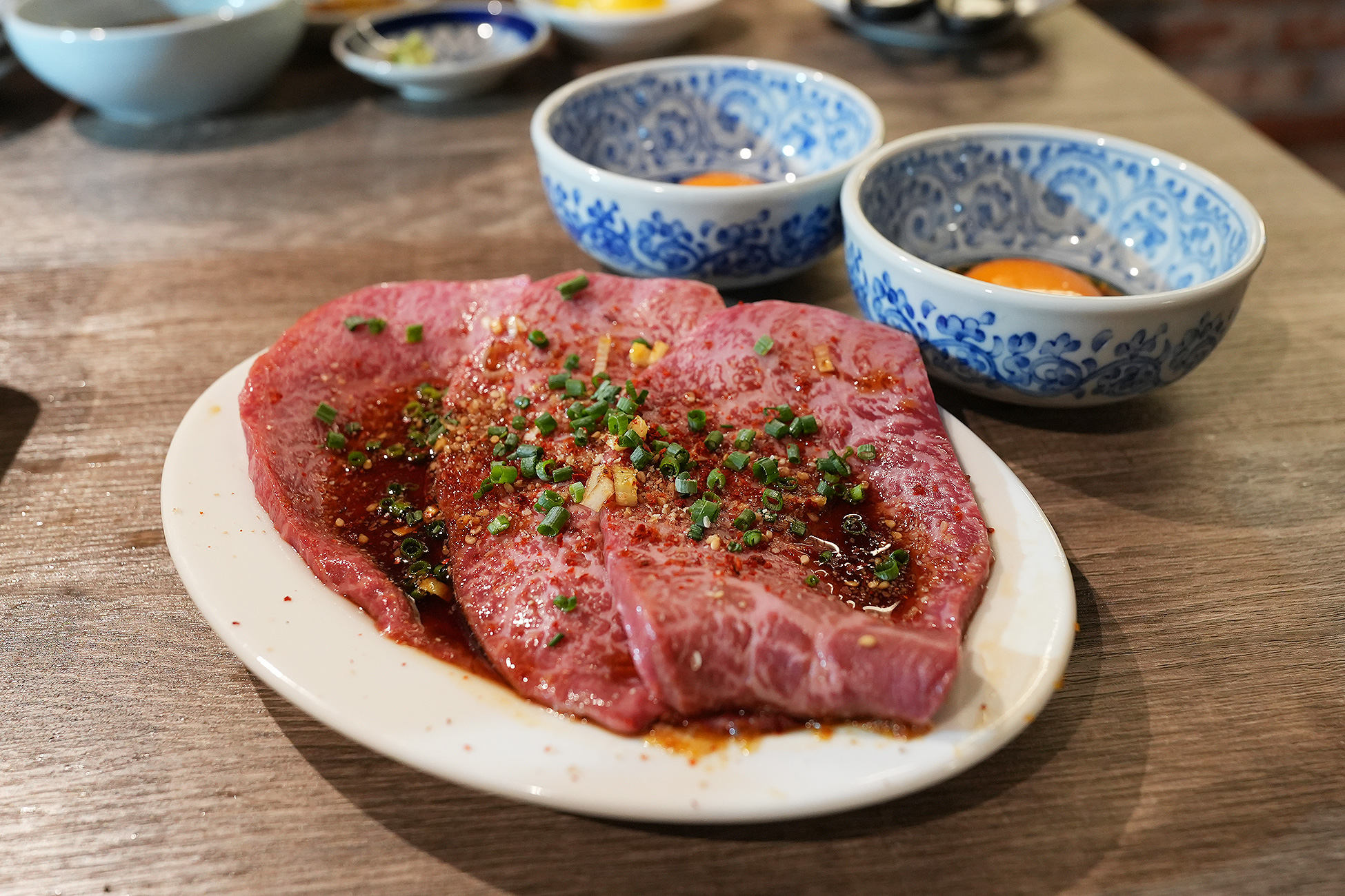 麻布苑のシンシン。薄切りの赤身にタレと唐辛子、万能ねぎ、にんにくがのり、奥に卵黄が2つ用意されている