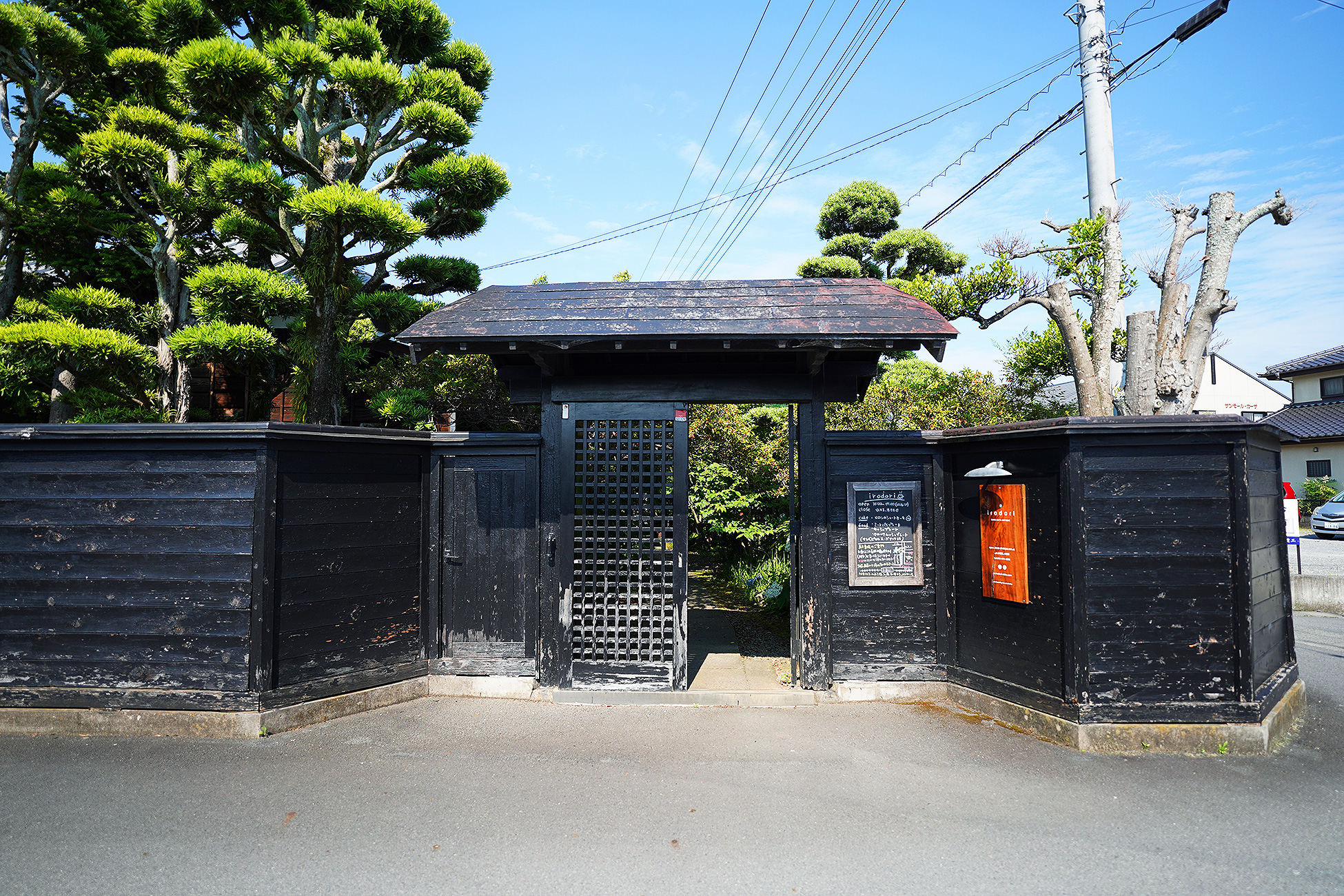 irodoriの黒い板塀と門。手入れされた松が塀の向こうに見える