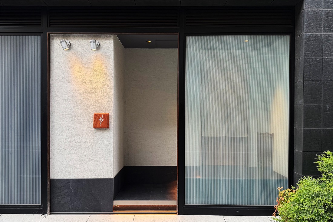 鴨ゆきの外観。石とテクスチャーのある壁に、小さな銅色の看板が掛かった控えめな入り口