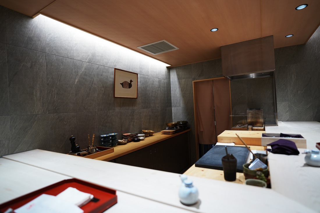 鴨ゆきの店内。グレーの石壁と木の天井、白木のカウンター。壁には鴨の絵が飾られている