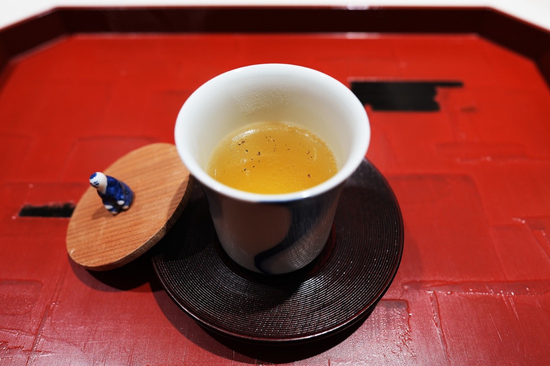 黒い器に注がれた、澄んだ金色の鴨のコンソメ。木の蓋には小さな鴨の置物がのっている