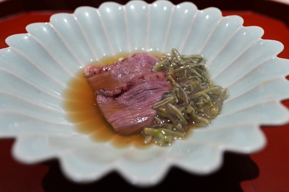 白い菊形の器に、出汁にくぐらせた鴨ロースと蓴菜、黄韮を盛った一皿