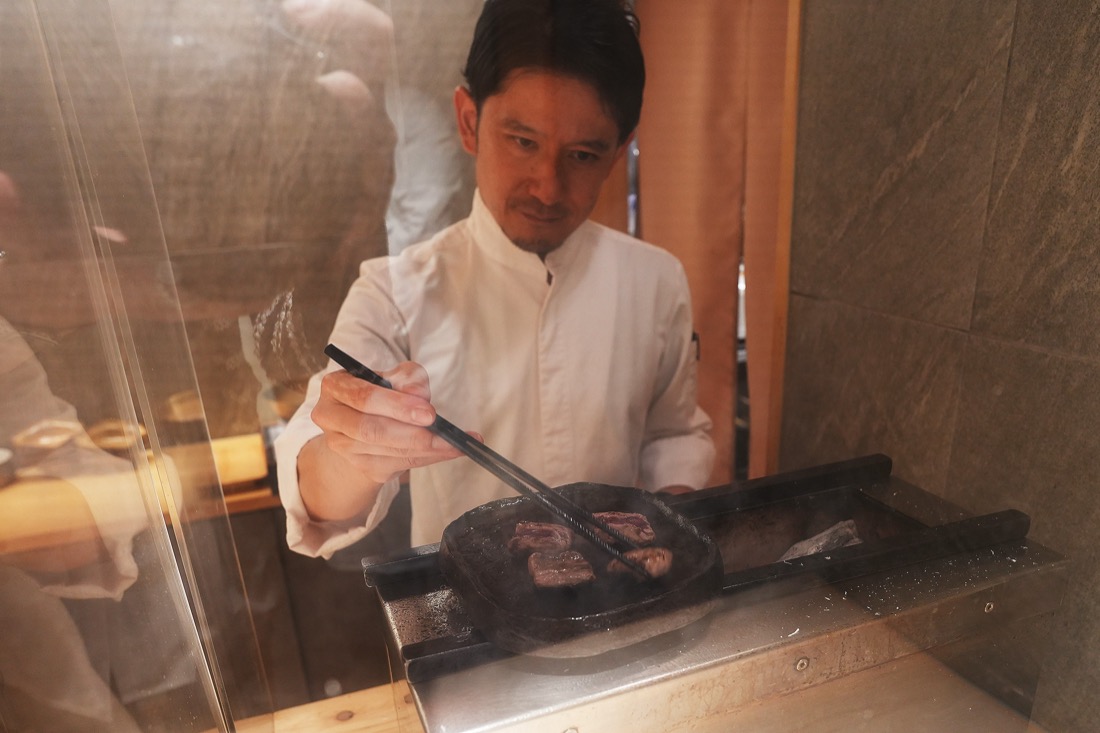 カウンター越しに、丸い玉鋼の鉄板で鴨を焼く北島シェフ