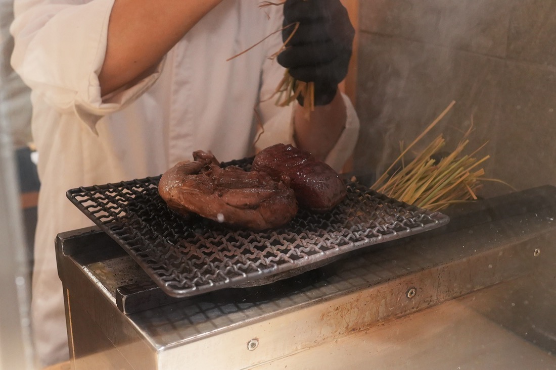 網にのせた鴨肉に、束ねた藁で火をあてる北島シェフ