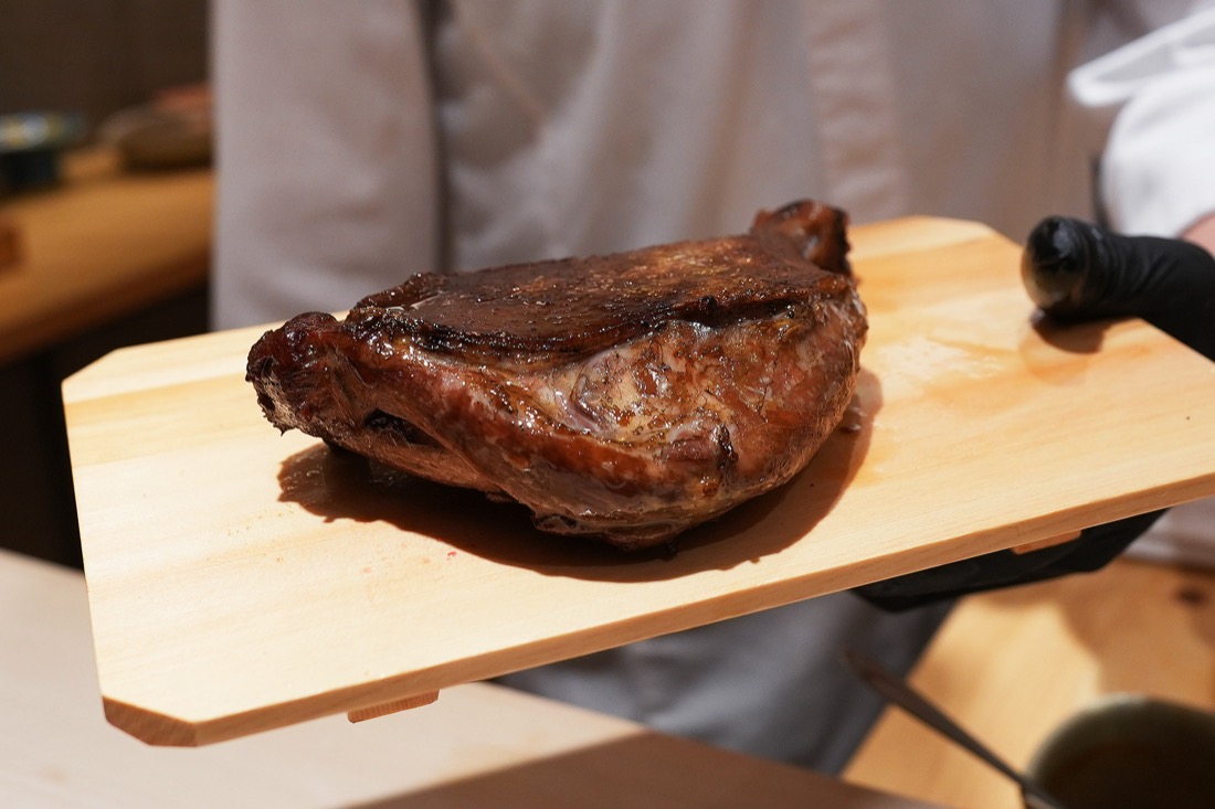 木のまな板にのせられた、こんがりと焼き上がった鴨の骨付きもも肉