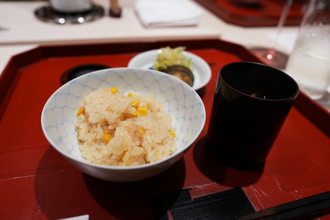網目模様の茶碗によそったとうもろこしご飯と、香の物、黒い漆の器