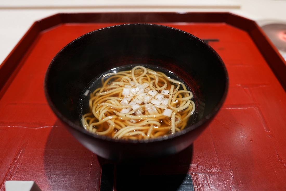 黒い漆の椀に盛られた、澄んだスープの鴨コンソメラーメン。刻んだ白葱がのっている