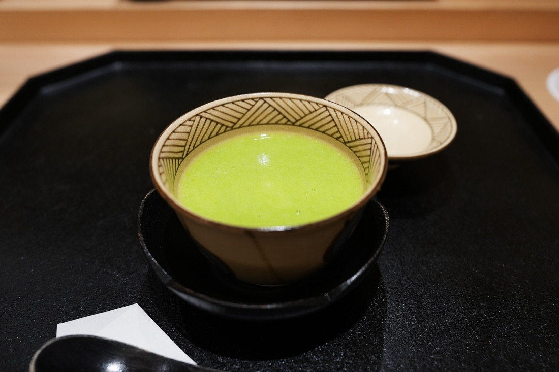 黄緑色のうすい豆の餡をかけた茶碗蒸し。黒い膳にのせられている