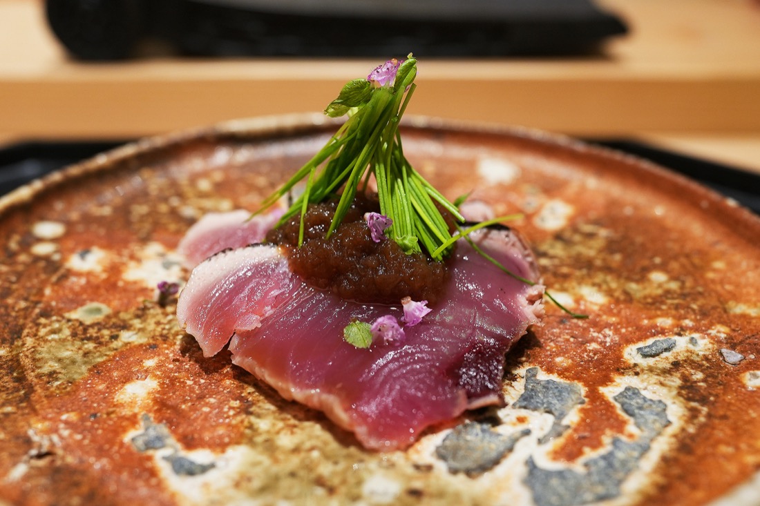 赤い大皿にのせられた初鰹の藁焼き。新玉葱のソースと芽葱が添えられている