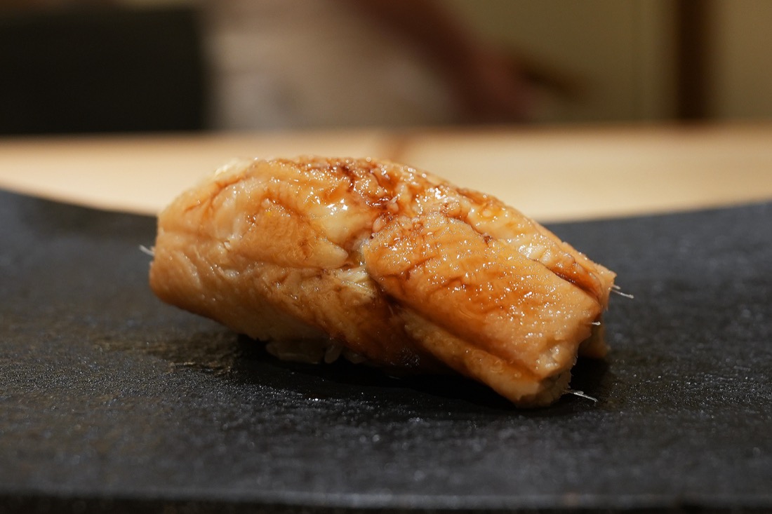 黒い付け台にのせられた、ふっくらと焼き上げた穴子の握り