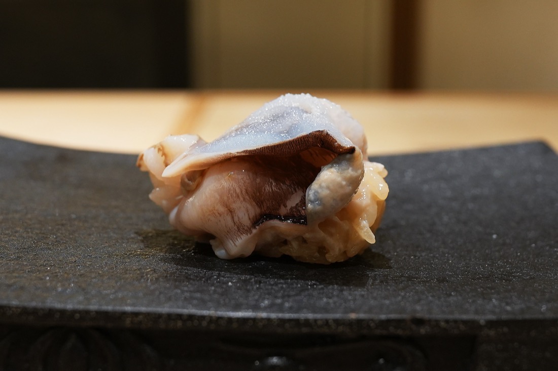 黒い付け台にのせられた鳥貝の握り。白い身に濃い茶色のヒダが走っている