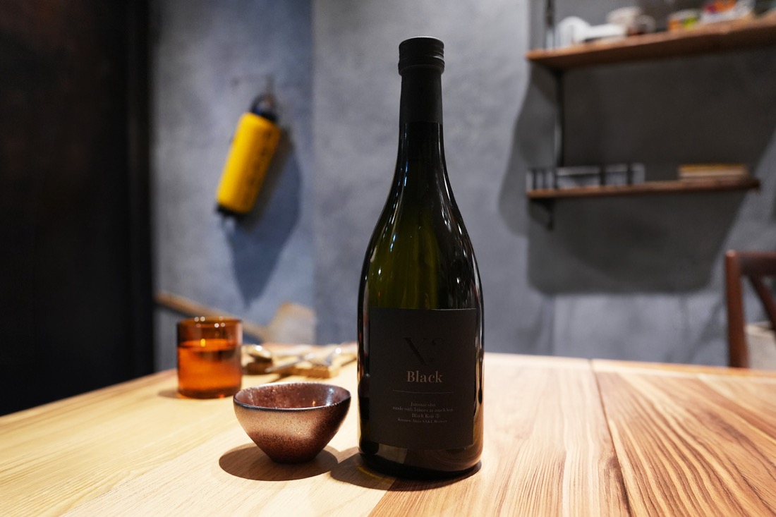 黒いラベルの日本酒「X3 Black」のボトルと、陶器のぐい呑み