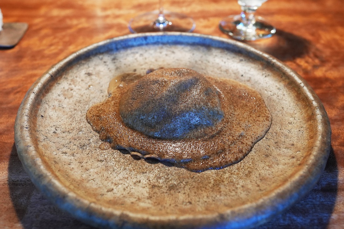 青い縁の陶器の皿にのせられた、どんぐり粉のラビオリとポルチーニのソース