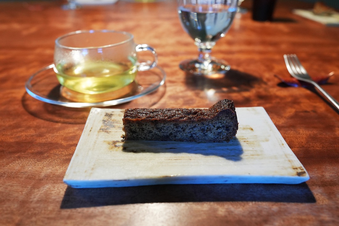 白木の板にのせられたヘーゼルナッツケーキと、ガラスのカップに入ったハーブティー
