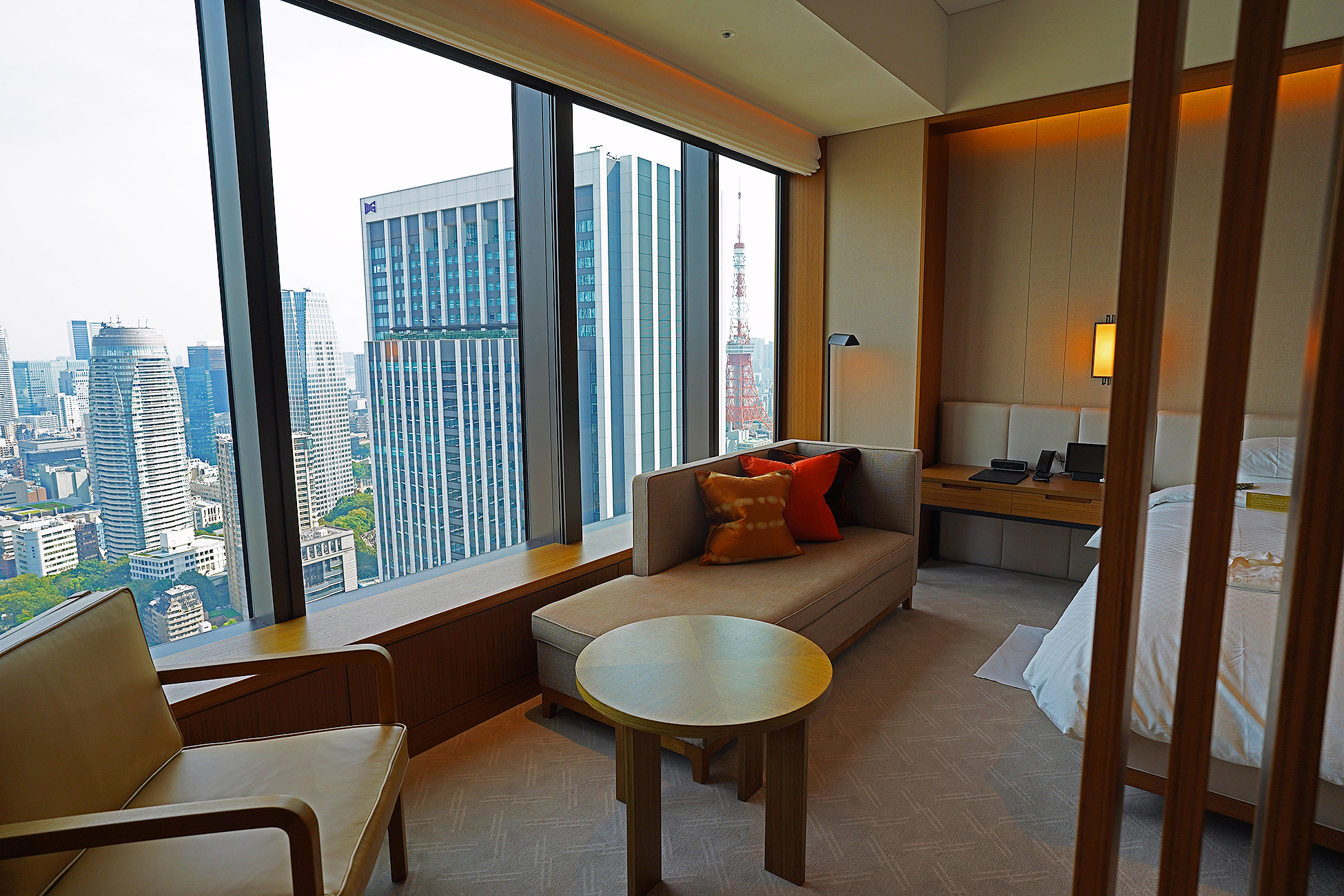 The Okura Tokyoプレステージルームの窓際。造作のベンチソファに朱色の絞りクッションが置かれ、窓の右端に東京タワーが見える