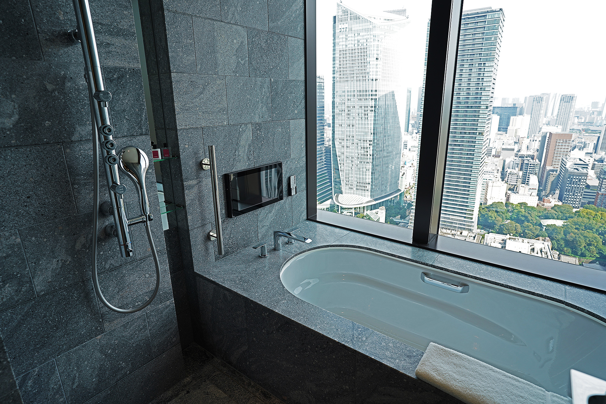The Okura Tokyoプレステージルームのバスタブ。窓に面して浴槽が据えられ、石壁にテレビが埋め込まれている
