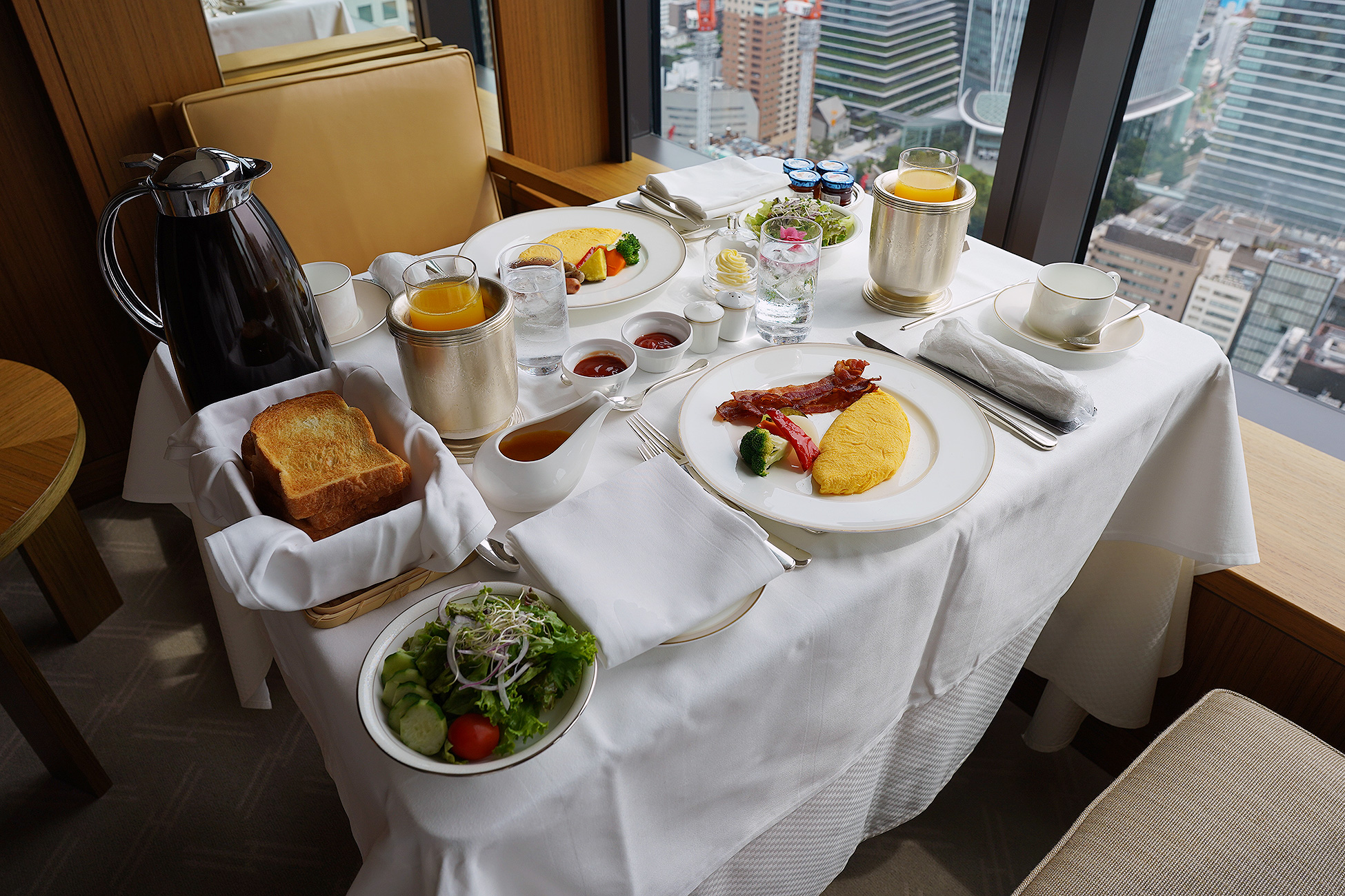 The Okura Tokyoのルームサービス朝食の全景。オムレツ、トースト、サラダ、ジュース、コーヒーが窓辺のテーブルに並ぶ