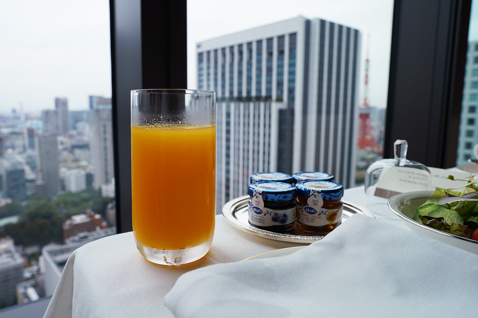 The Okura Tokyoのルームサービス朝食のオレンジジュース。銀の器に入ったグラスが窓辺に置かれている