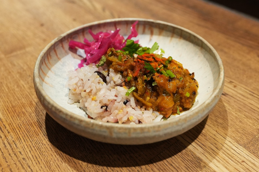 器に盛られた、雑穀ごはんのスパイスカレー。上に紫の漬物がのっている
