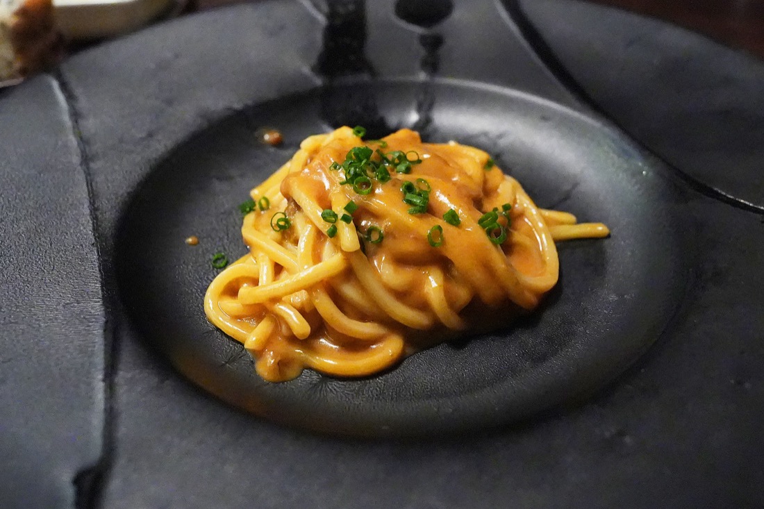 黒い皿に盛られた、雲丹のソースが絡んだオレンジ色の温かいパスタ