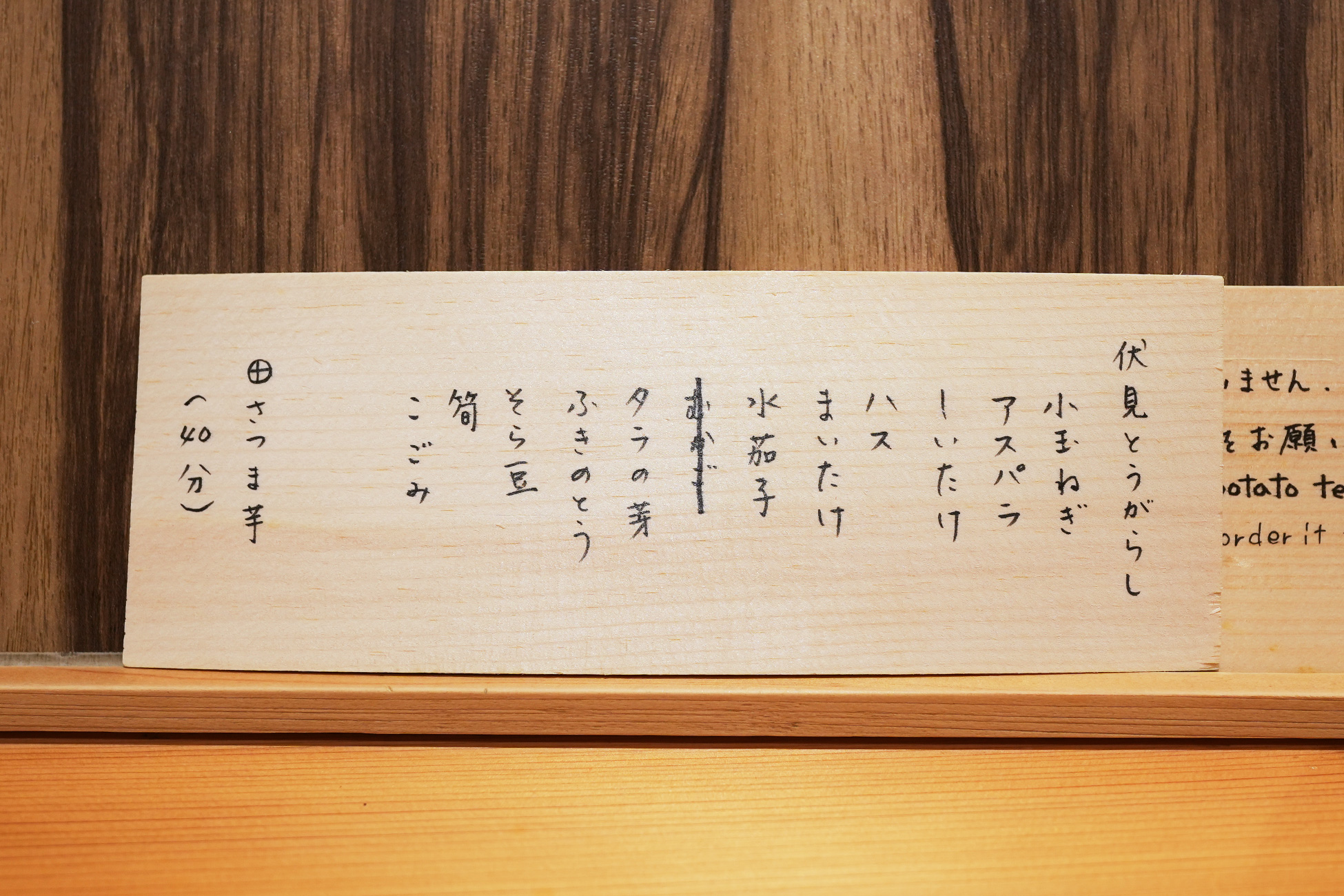 木の札の裏面に書かれた野菜の品書き。伏見とうがらし、アスパラ、まいたけ、水茄子、タラの芽、ふきのとう、そら豆、筍、こごみ、さつま芋（40分）