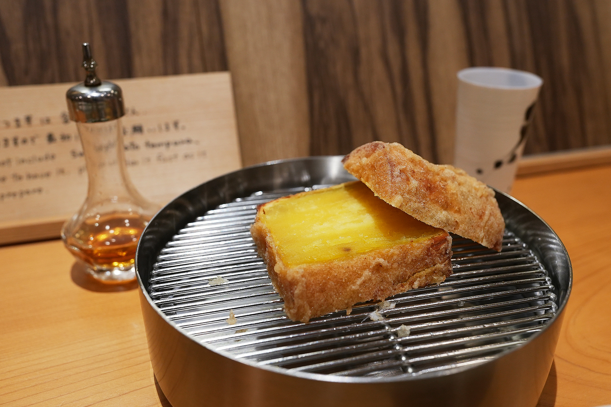 厚切りのさつまいもの天ぷら。断面は鮮やかな黄色で、奥にブランデーの小瓶が見える