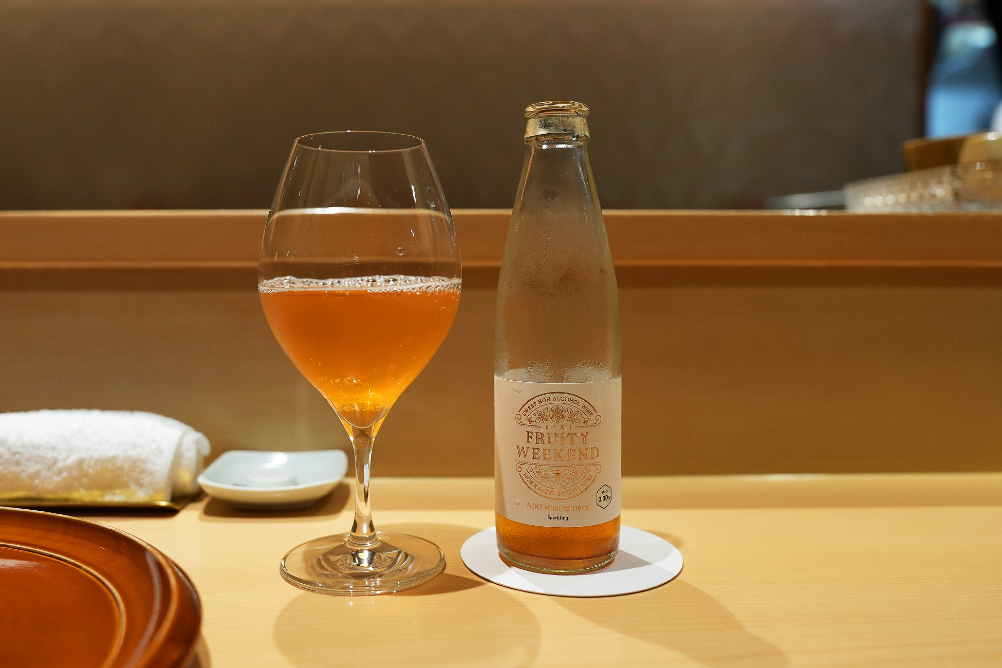 グラスに注がれた淡いオレンジ色のノンアルコールスパークリングと、NIKI Hills Winery のボトル