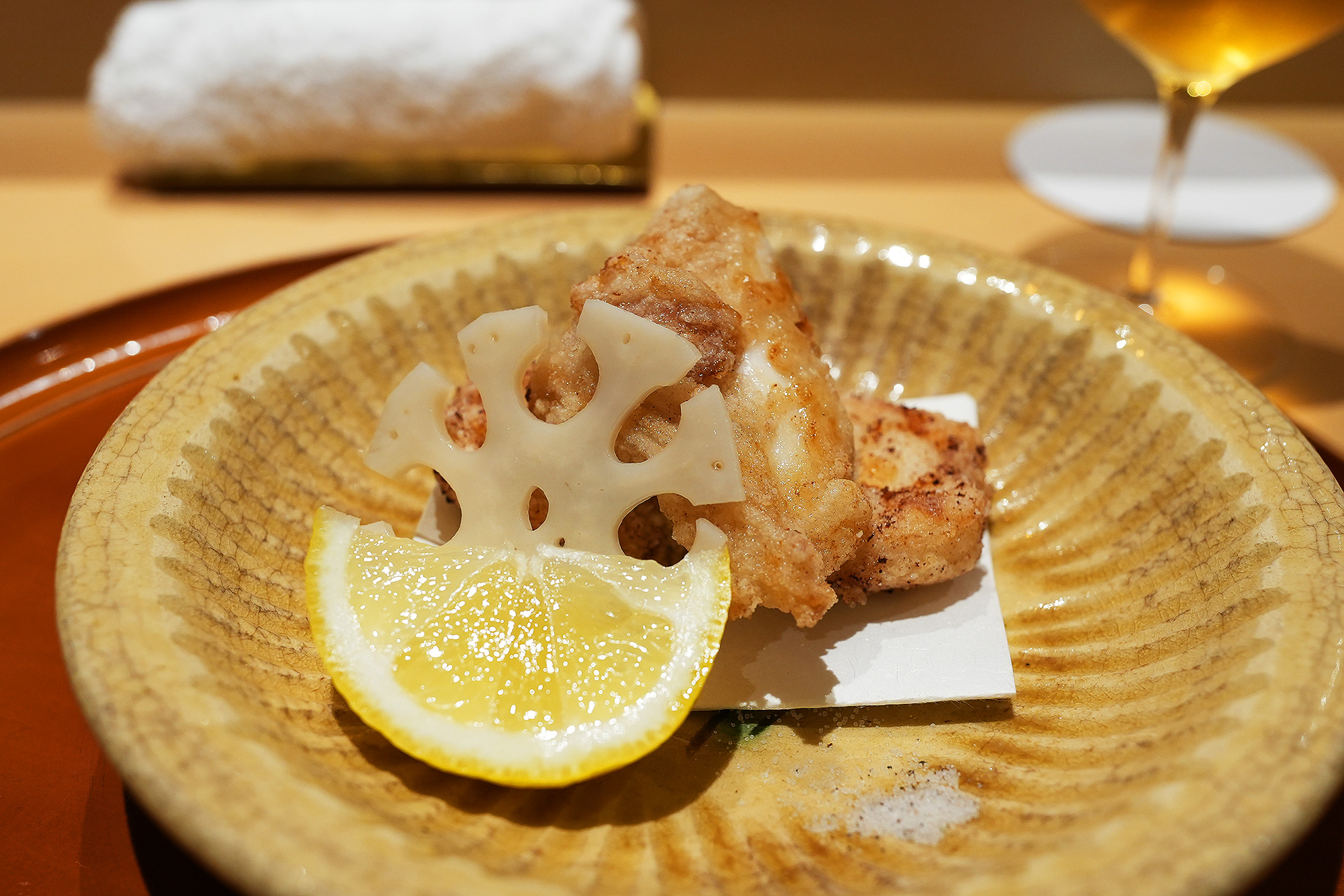 黄色い器に盛られた虎河豚の竜田揚げ、蓮根のチップとレモンを添えて