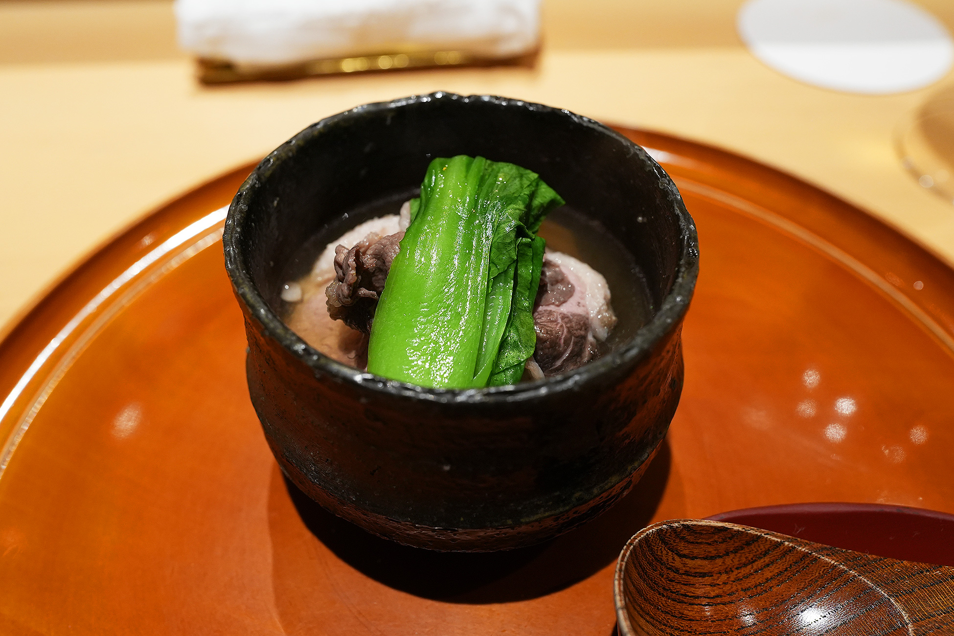 黒い器によそわれた鍋。青梗菜と豆腐、合鴨とツキノワグマの肉が澄んだ出汁に浸かっている