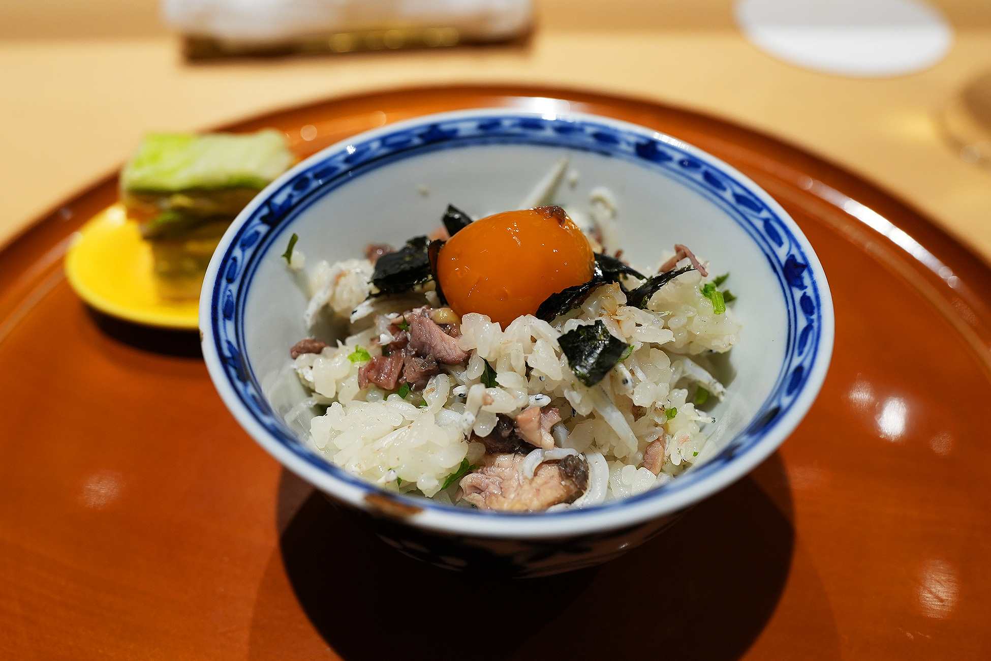 染付の器によそった土鍋ご飯。すっぽん、シラス、海苔の上に卵黄がのっている