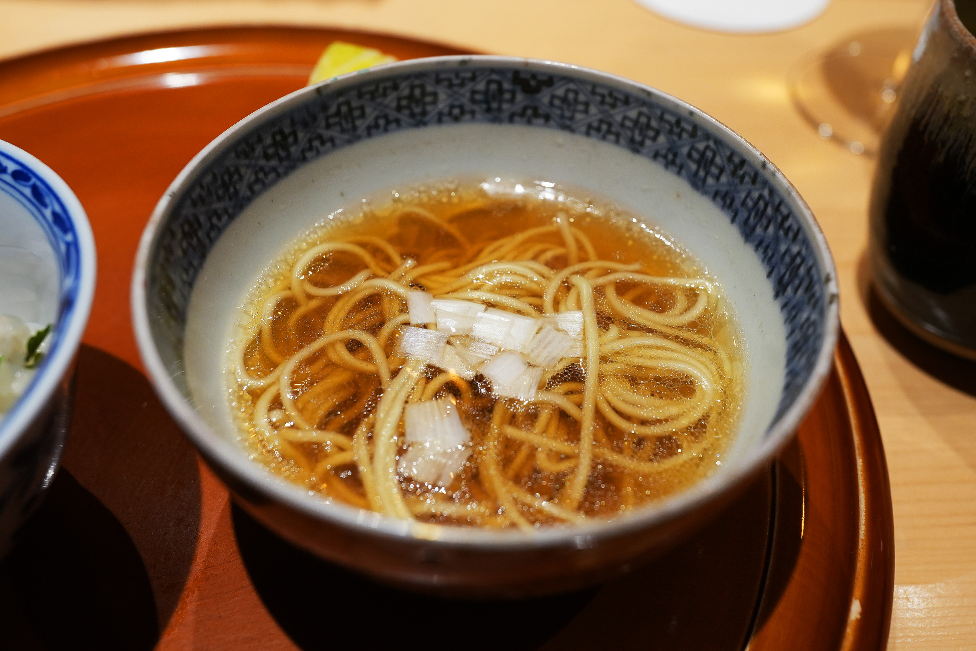染付の椀に、澄んだ琥珀色の出汁と細麺、白髪ねぎをのせたラーメン