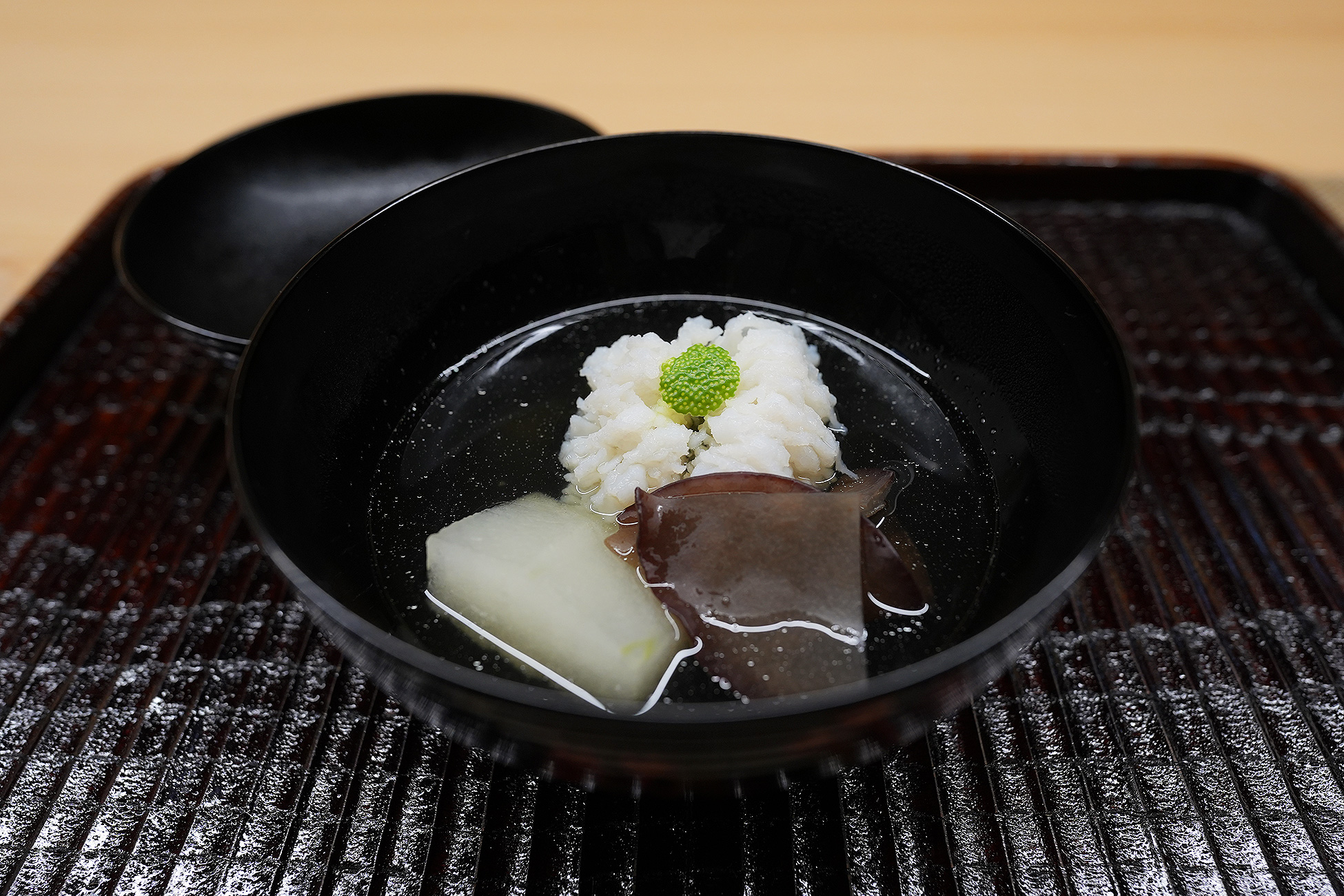 黒い椀に澄んだ出汁。白く開いた鱧、黒い木耳、白い蕪が入っている
