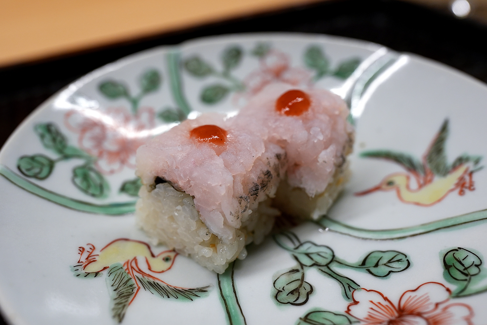 色絵の皿にのせた鱧の押し鮨2切れ。白く細かくほぐれた鱧の身が酢飯をおおい、赤い点がひとつずつのっている