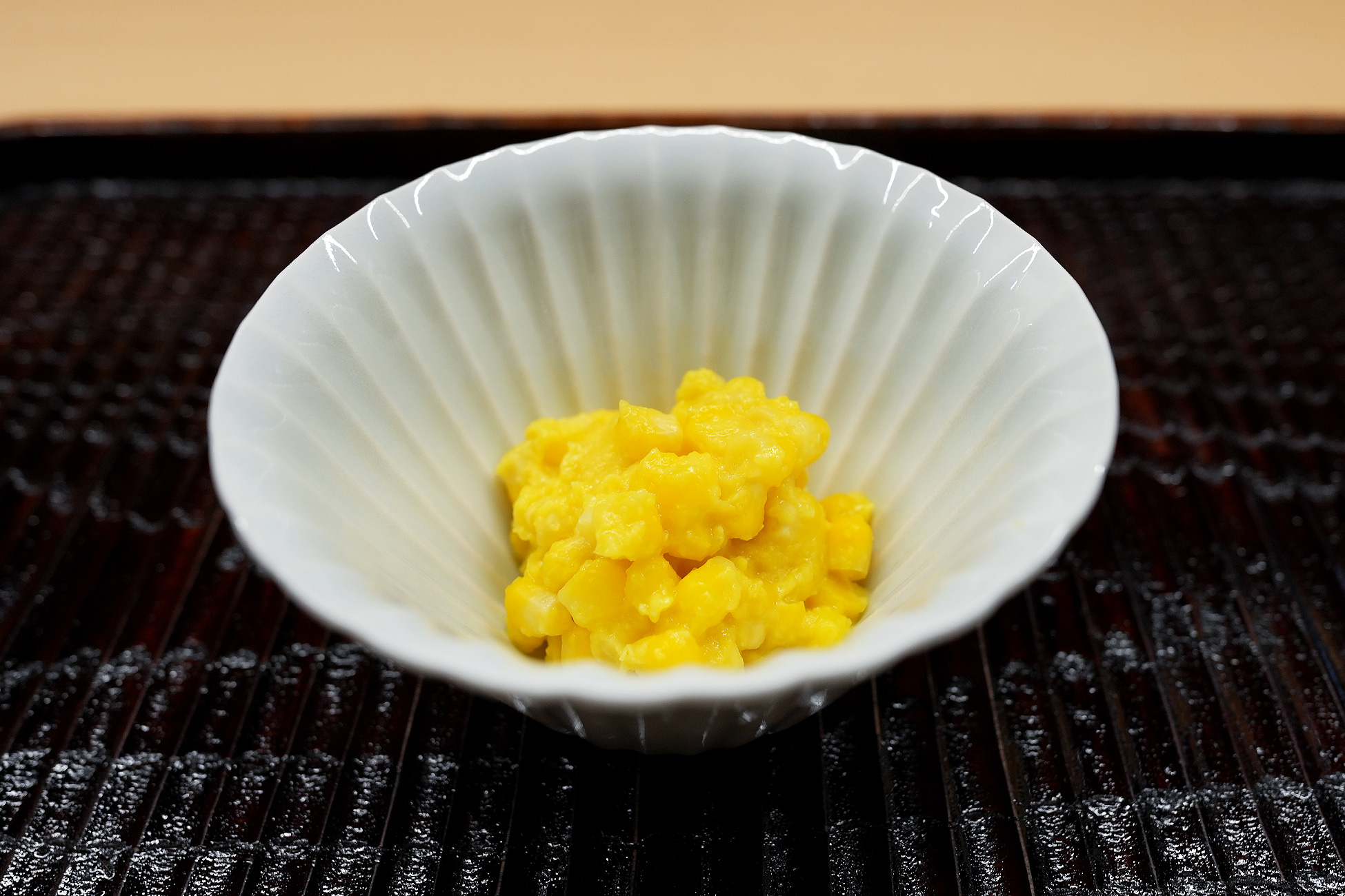 白い菊形の小鉢に盛られた、とうもろこしの粒をとうもろこしのペーストで和えた一品