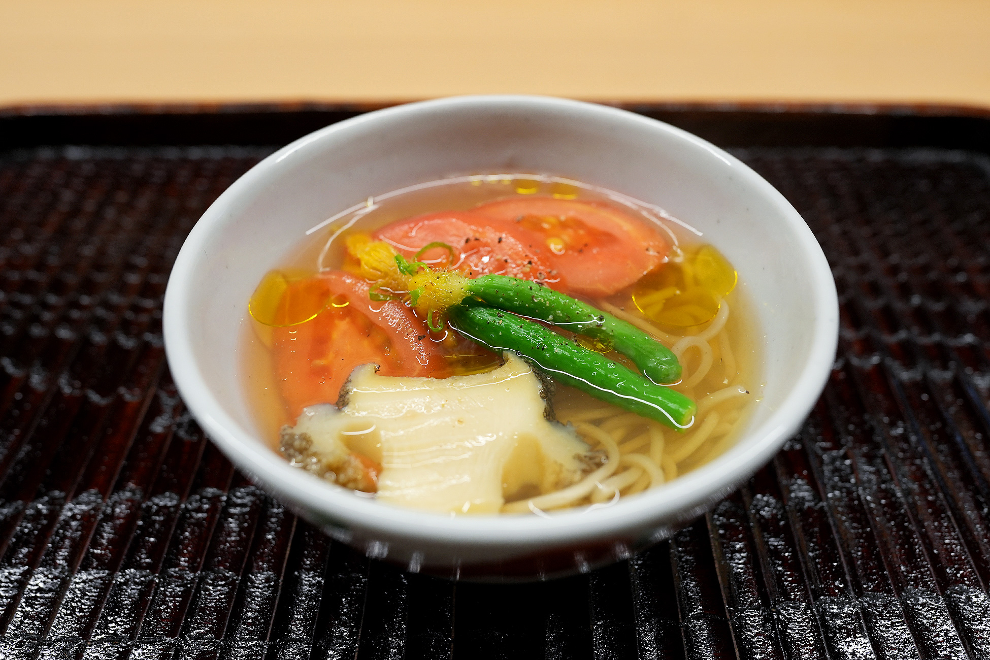 白い器に澄んだスープと細麺、トマトのスライス、鮑、いんげんが入ったラーメン