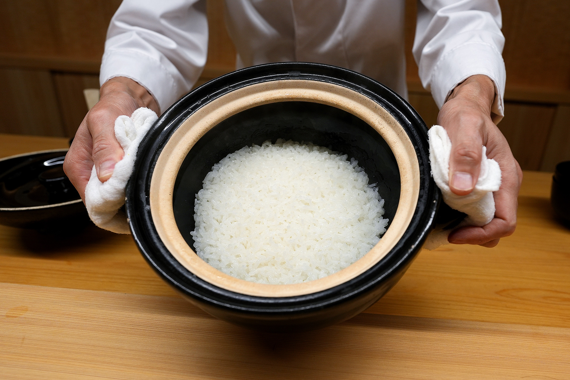 土鍋いっぱいに炊き上がった白米を、料理人が両手で持って見せているところ