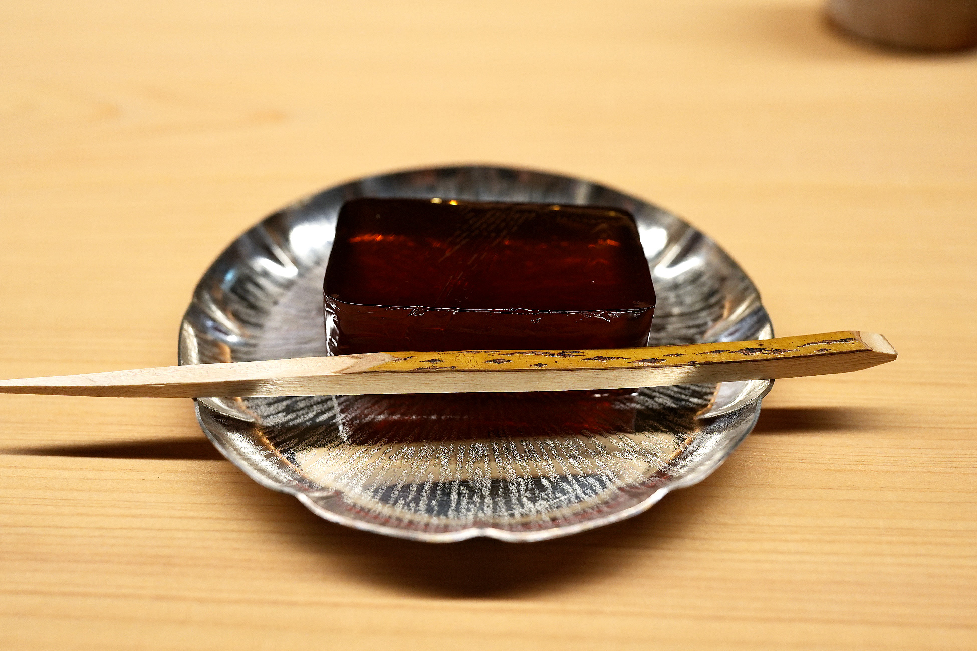 銀色の皿にのせた琥珀色の寒天菓子「したたり」。竹の菓子切りが添えられている