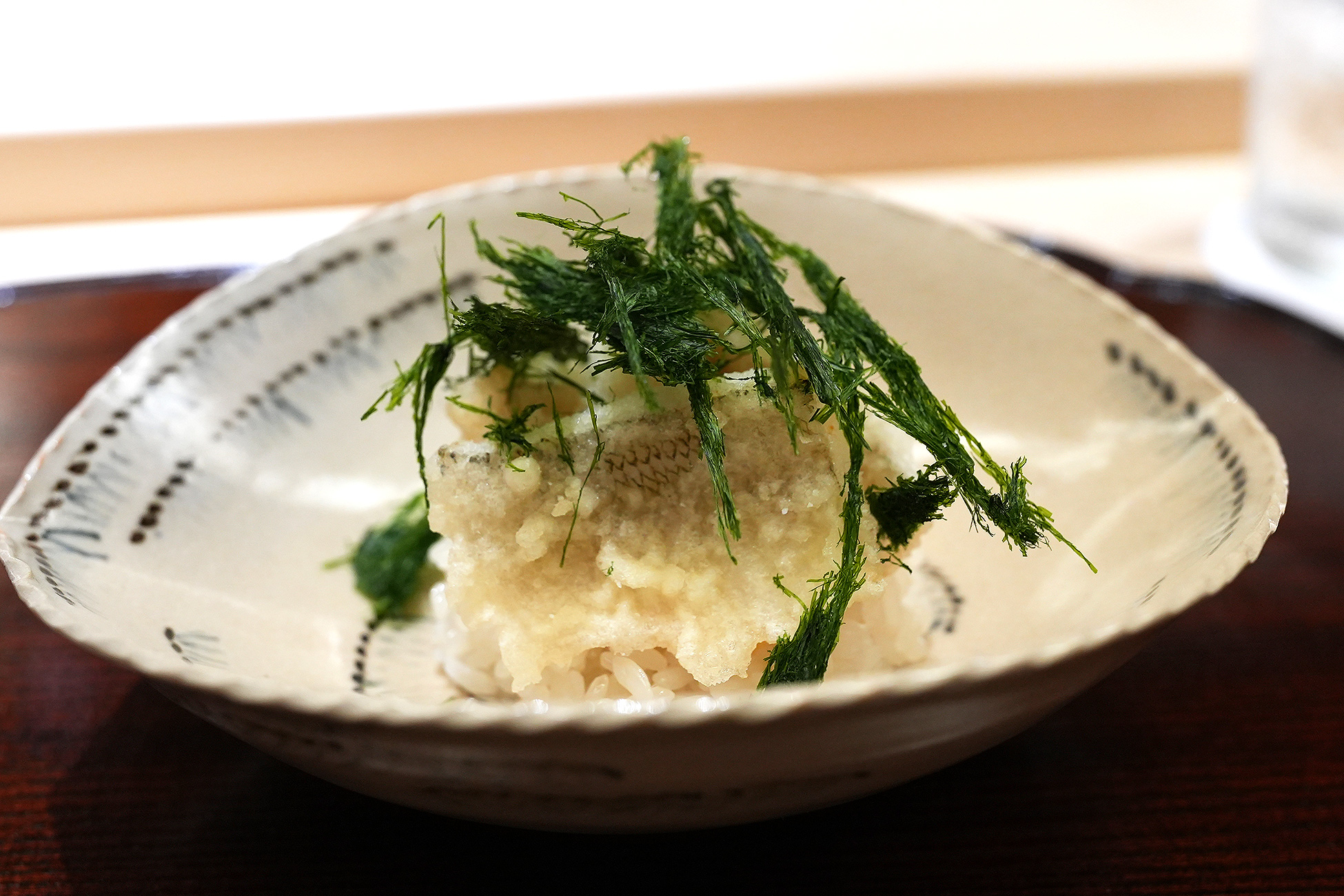 飯蒸しの上に鱚の天ぷらを重ね、青い海苔をあしらった一皿
