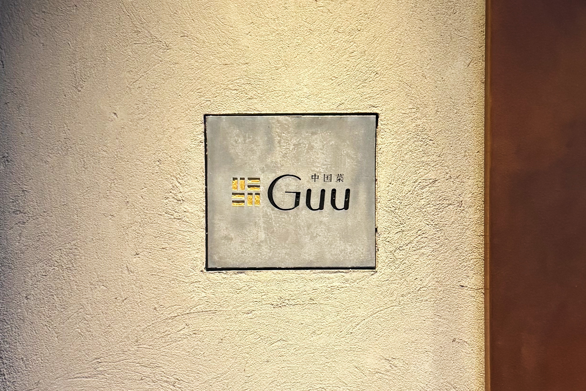 塗り壁にはめ込まれたコンクリートの看板。「中国菜 Guu」の文字が入っている