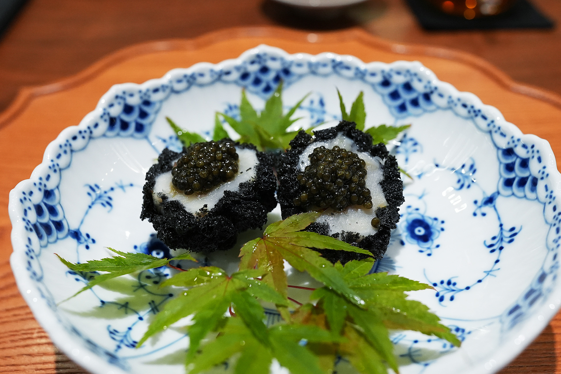 染付の皿にのせた、竹炭で黒くした揚げパン2つ。白い帆立の上にキャビアがのり、青もみじが添えられている