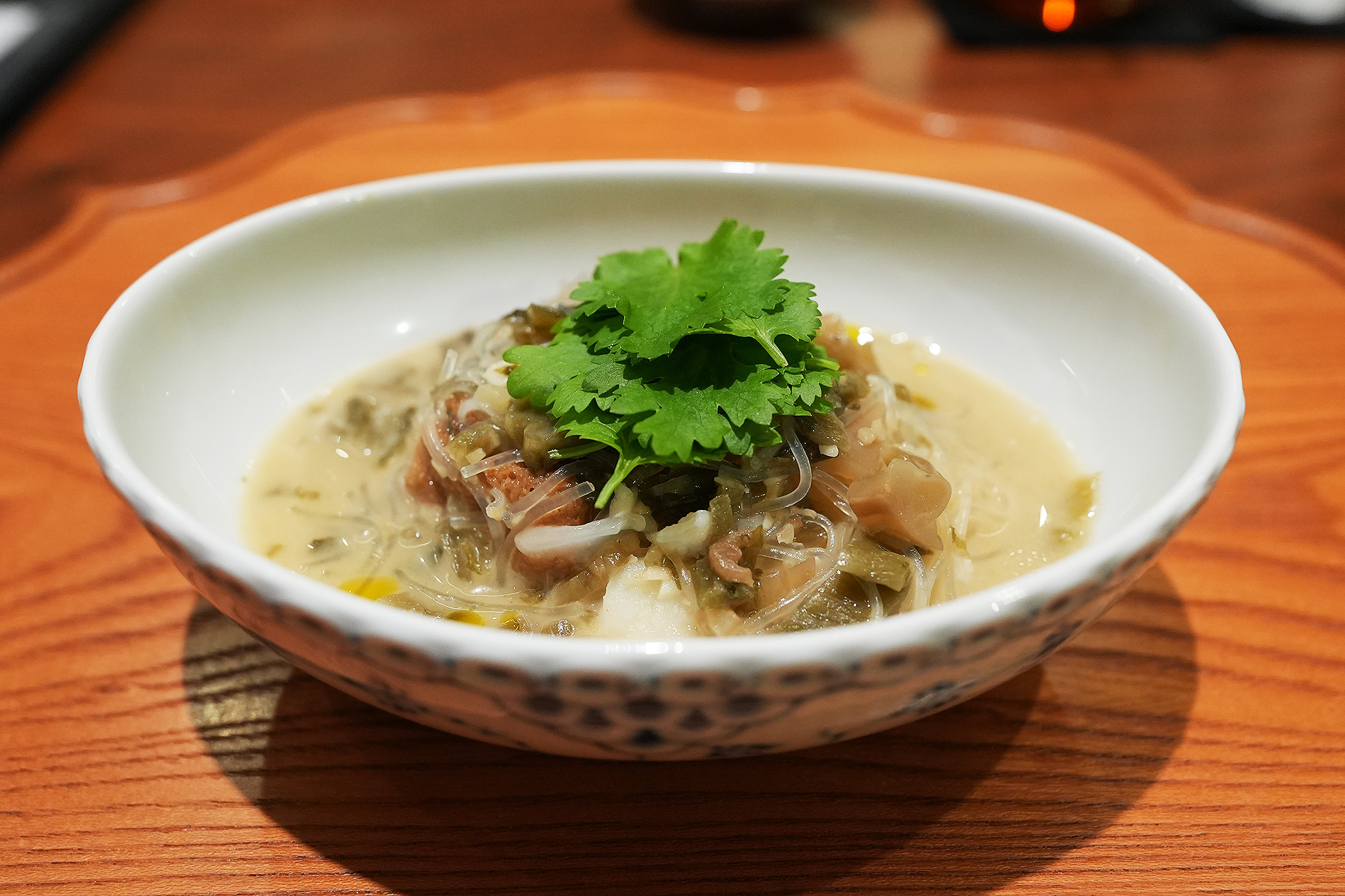 白い鉢によそわれた白湯スープの煮込み。春雨、酸菜、クエの身、豆腐が入り、上にパクチーがのっている