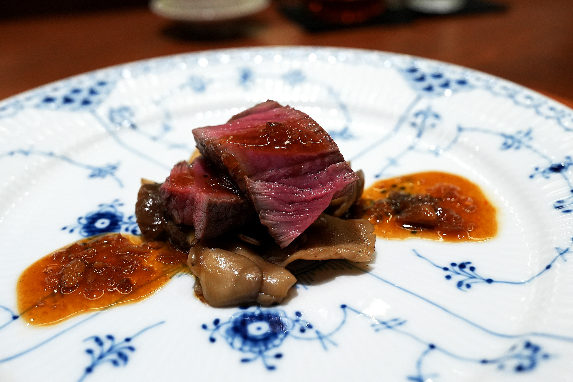 染付の皿に、中心まで赤みの残る和牛ヒレ肉のスライス。下に茸、まわりに赤茶色のソースが敷かれている