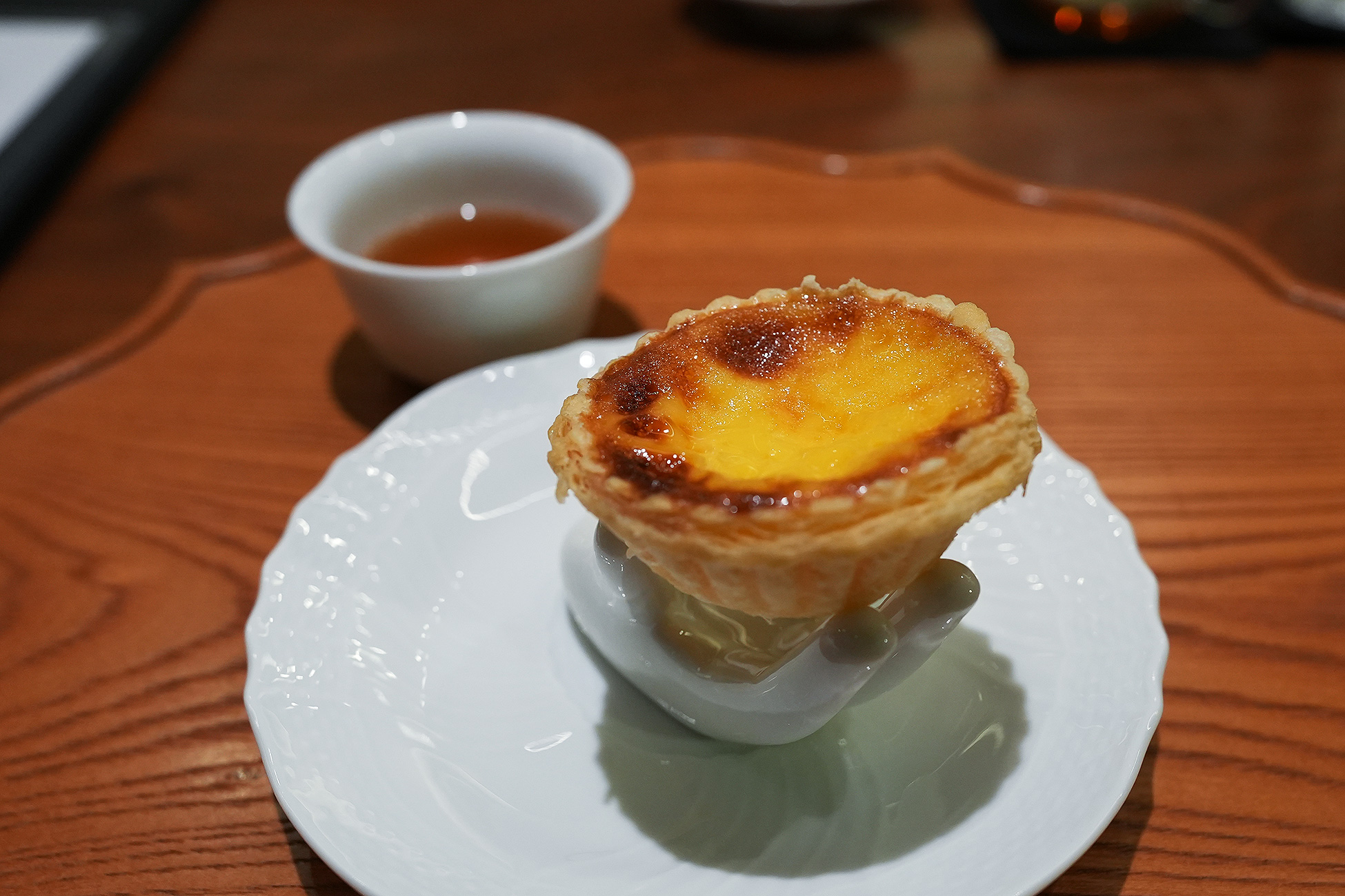 青磁の台にのせた焼き立てのエッグタルト。表面に焼き色がつき、横には金木犀のお茶が置かれている