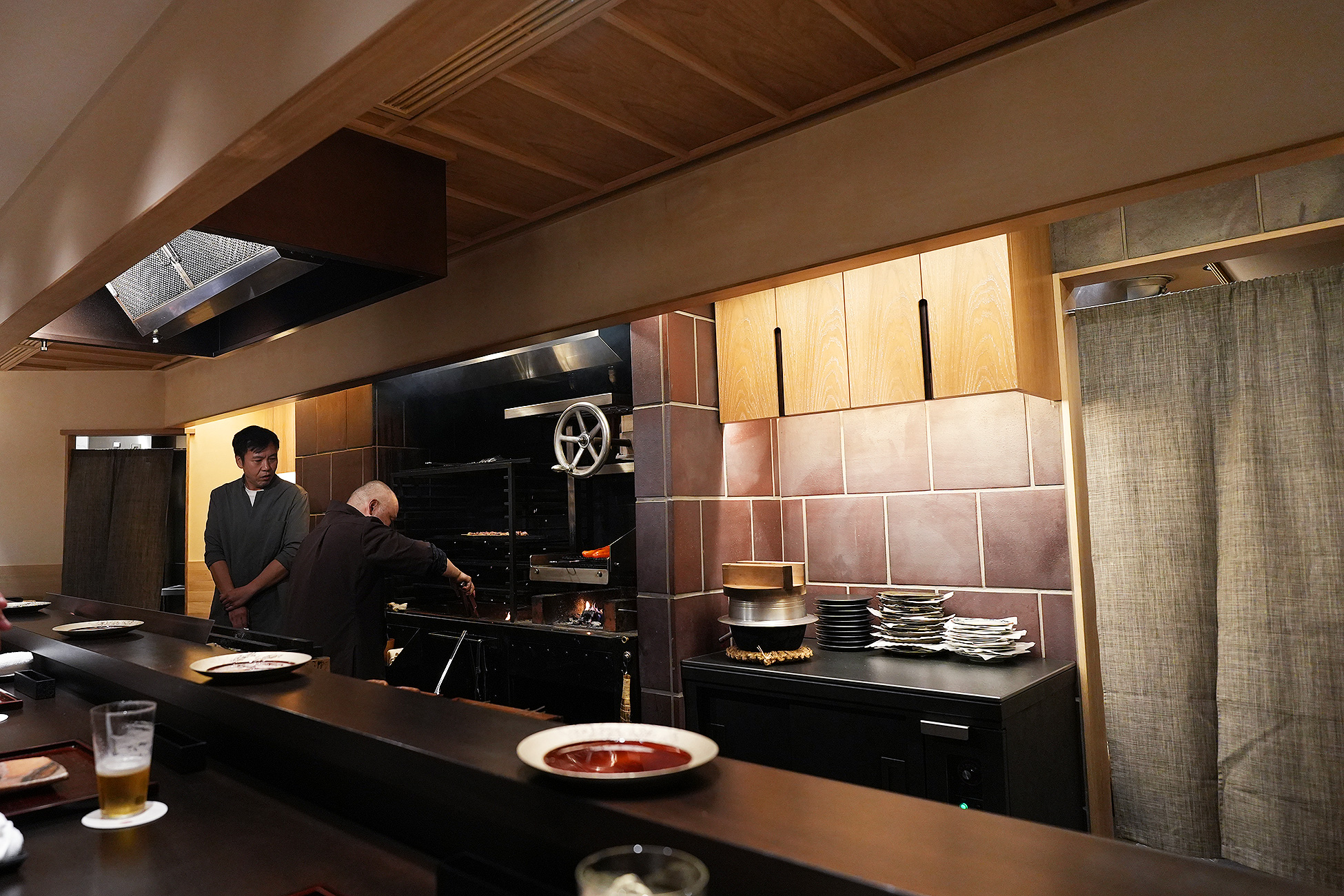 ひき田の店内。一枚板のカウンターの向こうが焼き場になっていて、奥で炎が上がっている。右手には和紙の暖簾がかかる