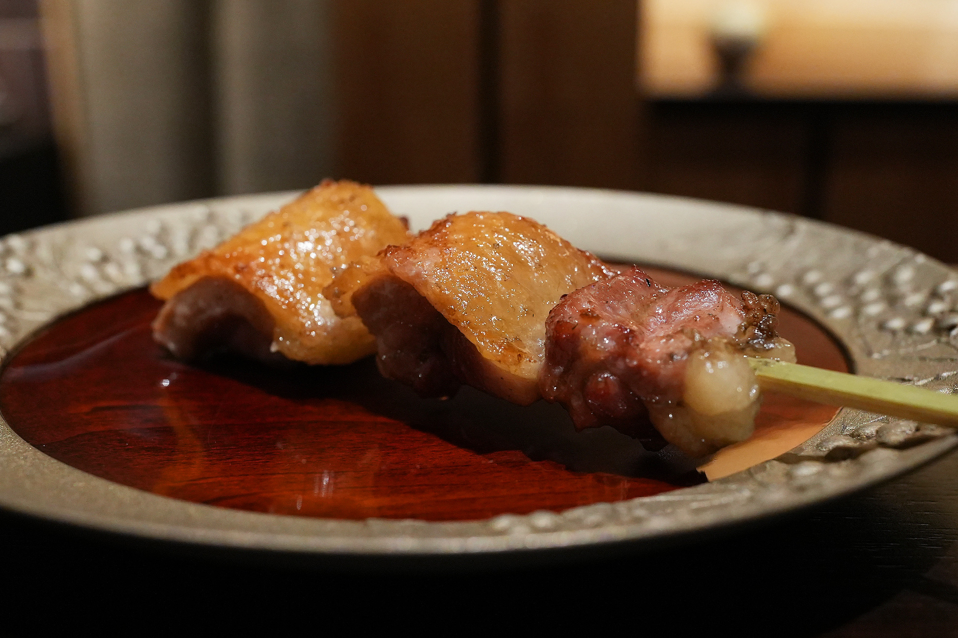 銀色の縁取りの皿に、薪焼きにした比内地鶏のもも肉が2切れ。皮目に焼き色がつき、手前に赤身の部位が添えられている