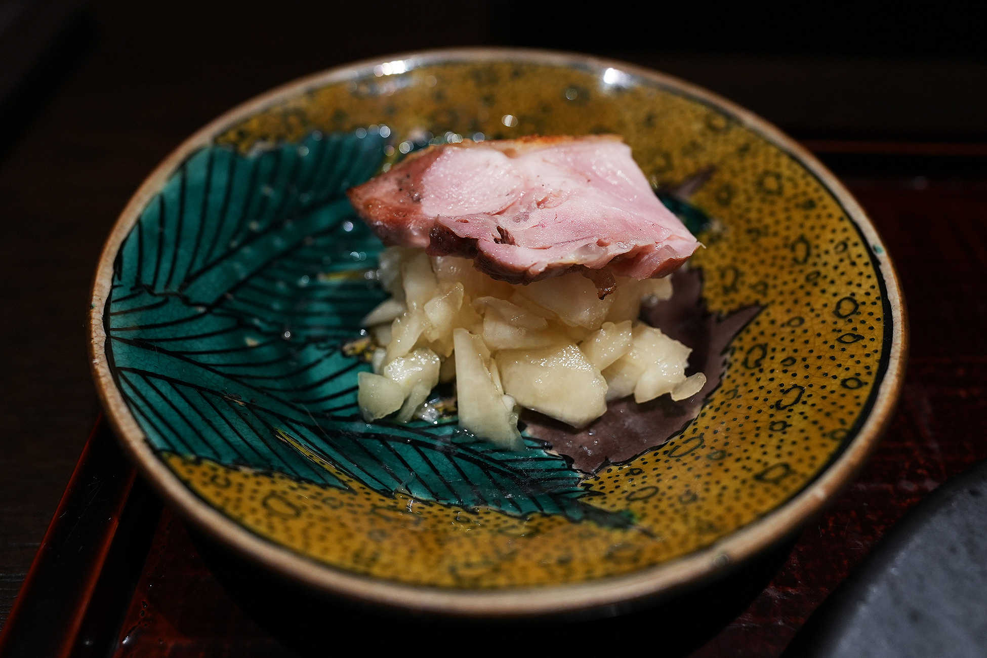 黄色と緑の葉模様の皿。紫の葉を敷いた上に粗くおろした大根が盛られ、焼いた鶏肉が一切れのせてある