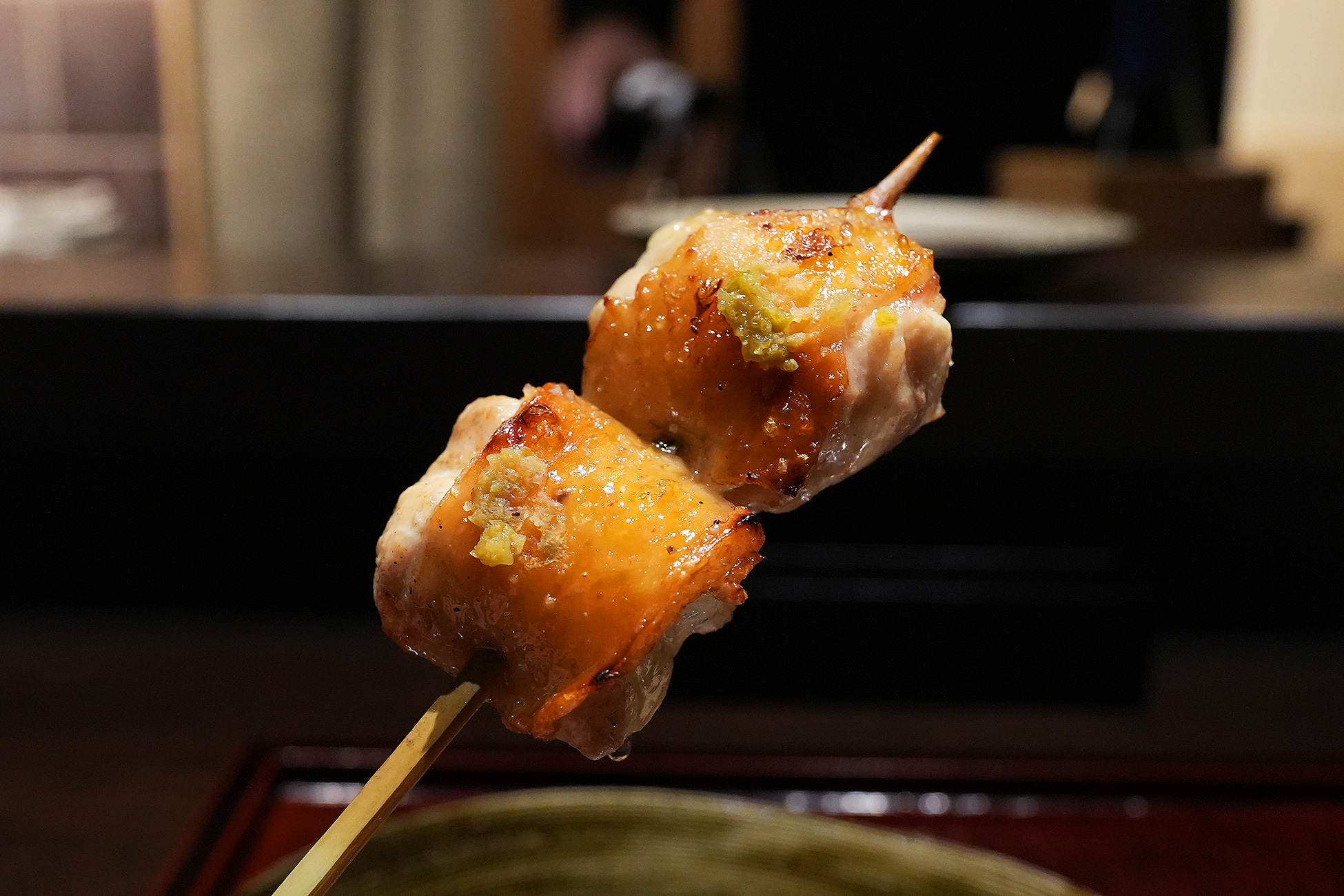 手に持った串に、皮目をこんがり焼いた鶏肉が2切れ。それぞれの上に黄色い薬味がのせてある